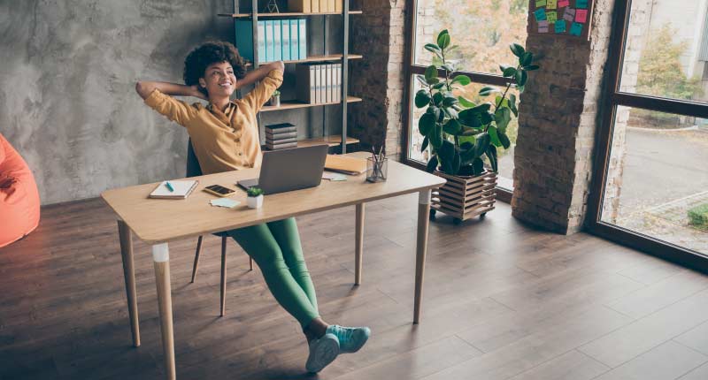  A woman wearing a yellow shirt relaxing with her hands behind her back at her workstation