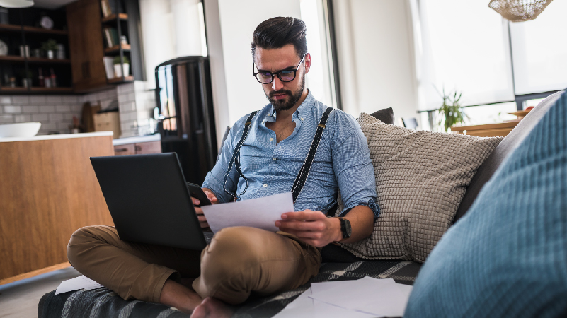 man using smartphone and laptop while sitting on the sofa at home