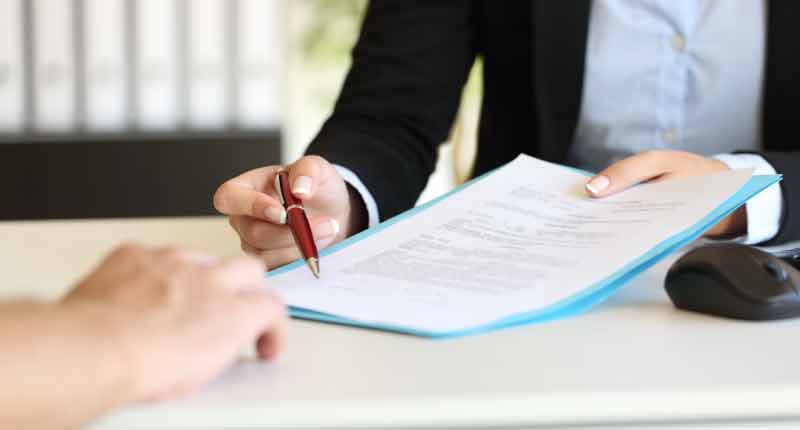 Close-up of an executive’s hands holding a pen and contract, showing employee where to sign it