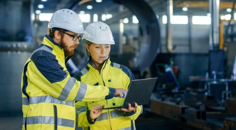 Male and female industrial engineers in hard hats discuss new projects while using laptops